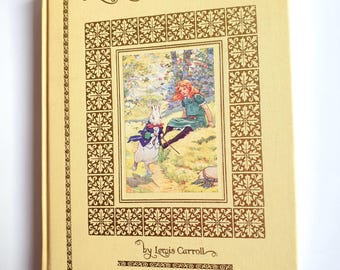 Puede incluir: Un libro antiguo de tapa dura titulado "Alicia en el país de las maravillas". La portada es de color amarillo claro con letras doradas y bordes decorativos. La ilustración representa a Alicia y al Conejo Blanco. El libro forma parte de la serie "Illustrated Classics".
