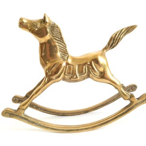 May include: A gold-coloured rocking horse figurine with a detailed design. The horse is on a rocking base.