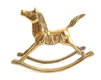Puede incluir: Una figurita de caballo de balancín de color dorado con un diseño detallado. El caballo está sobre una base de balancín.