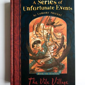 May include: A hardback book titled "A Series of Unfortunate Events" by Lemony Snicket. The cover shows an illustration of children and crows, with the title "The Vile Village" at the bottom. The spine is red with a textured design.