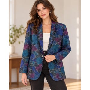 May include: A long-sleeve blazer featuring a vibrant floral pattern in shades of deep blue, teal, and purple. The blazer has a notched lapel, a single-button front closure, and is worn over a plain white top and dark-colored pants.