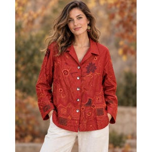 May include: A long-sleeved, button-down shirt in a deep rust-orange color. The shirt features intricate tonal embroidery with floral and geometric patterns throughout the fabric, a classic collar, and a straight hemline with a buttoned front closure.
