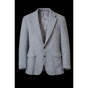 Op de afbeelding: Een lichtgrijze blazer met twee voorzakken en een sluiting met twee knopen. De jas heeft een revers met inkeping en een gewatteerde voering. De blazer is gemaakt van een textuurstof en wordt tegen een zwarte achtergrond getoond.