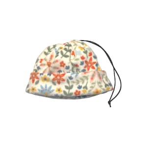 May include: A white fleece beanie hat with a floral pattern in red, orange, yellow, and blue. The hat has a drawstring and is suitable for cold weather. The hat is a small size.