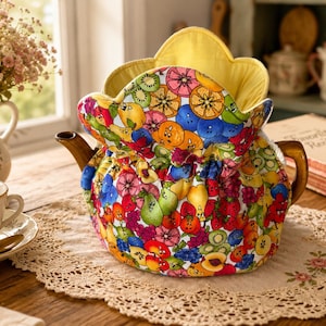 May include: A quilted fabric tea cozy featuring a vibrant, multi-colored pattern of cartoon-style fruits including pears, oranges, berries, and kiwi slices. The cozy has a scalloped top edge, a bright yellow interior lining, and a gathered base.