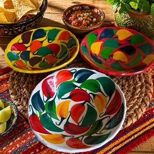 May include: A selection of vibrantly painted ceramic bowls featuring a chilli pepper motif. The bowls are in shades of yellow, red, and white. The image also shows a bowl of tortilla chips, salsa, and lime wedges, creating a celebratory atmosphere.