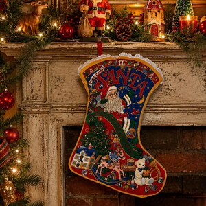 May include: A fabric Christmas stocking featuring a blue top section with the text Here Comes Santa in red letters. The main body displays a detailed illustration of Santa Claus, a decorated tree, a toy house, a rocking horse, and a teddy bear.