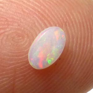 May include: A white oval opal gemstone with iridescent rainbow flashes.
