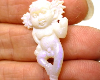 May include: A white opal carved into the shape of a cherub with iridescent purple and blue hues. The cherub is standing with its arms outstretched and has a playful expression on its face.