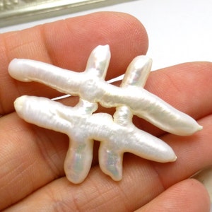 Könnte beinhalten: Ein weißer Barockperlenanhänger in Form eines stilisierten Buchstabens "#" mit irisierendem Schimmer.