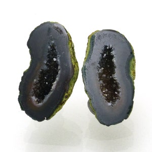 May include: Two halves of a geode, showcasing a dark gray interior filled with sparkling crystals. The outer edges are a mix of green and brown, creating a natural, organic aesthetic. The geode is cut to reveal the inner crystal formation.