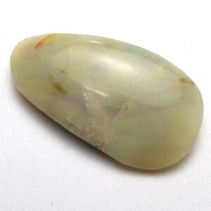 May include: A smooth, polished gemstone with a rounded shape. The stone has a translucent, creamy white base color with subtle yellow and brown inclusions. The surface is glossy, reflecting light and revealing internal patterns.