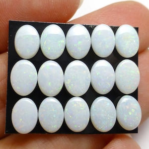 May include: A sheet of white opal cabochons, each oval shaped and set in a black backing. There are 15 cabochons in total, arranged in three rows of five.