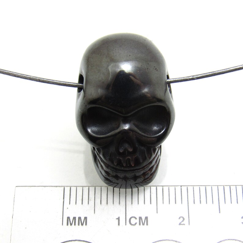 May include: Black skull bead pendant made of polished hematite. The bead is approximately 1 cm in diameter and has a hole drilled through the top for stringing.