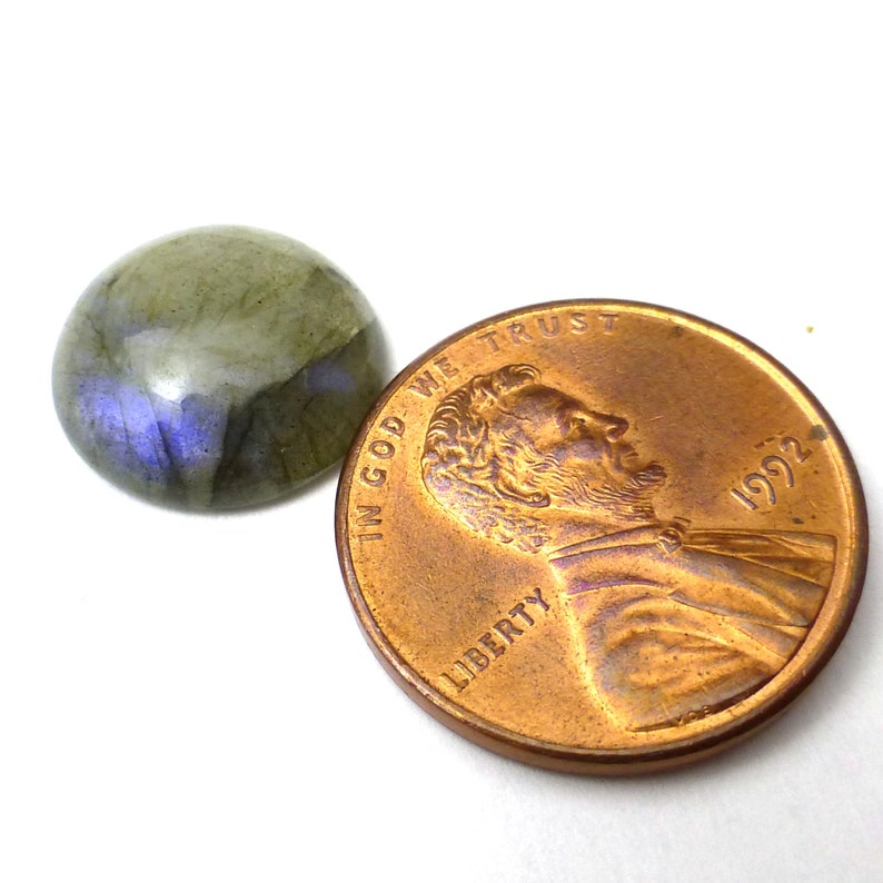 May include: A round, green and blue labradorite gemstone cabochon, approximately the size of a US penny. "In God We Trust" and "Liberty" are visible on the penny.
