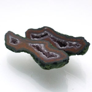 May include: Two halves of a geode with a green exterior and a purple and white crystal interior.