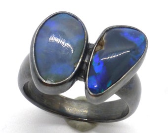 May include: A black metal ring with two oval-shaped blue opals set in the band.