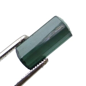 May include: A dark green gemstone with a rectangular shape, held in tweezers.