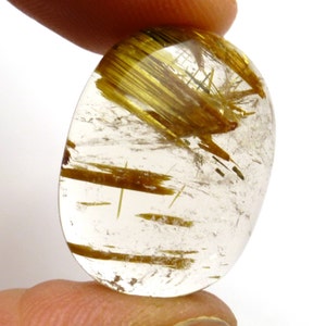 May include: A clear quartz cabochon with golden rutile inclusions. The rutile creates a shimmering effect within the stone.