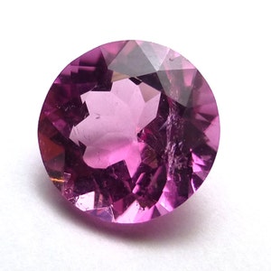 Può includere: Una pietra preziosa rotonda, sfaccettata, rosa con un motivo a forma di stella all'interno.