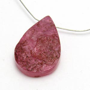 May include: A teardrop-shaped pendant made of pink and brown resin with a textured surface.