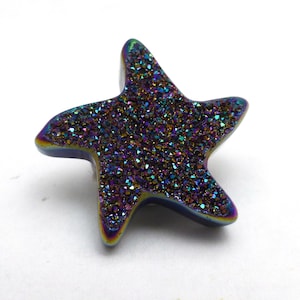 May include: A star-shaped decorative object with a shimmering, iridescent surface. The object features a spectrum of colors, including blues, purples, and greens, with a glittery texture. The edges are smooth and rounded.