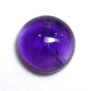 Könnte beinhalten: Ein runder, violetter Amethyst-Cabochon.