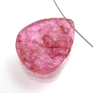 May include: A pink teardrop-shaped pendant made of natural ruby with a rough, textured surface.