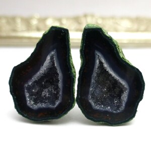 May include: Two halves of a geode with a dark purple and white crystal interior. The exterior is a dark green color.