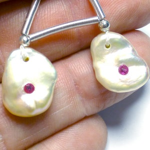 May include: Two white baroque pearls with pink gemstones set in the center, hanging from a silver chain.