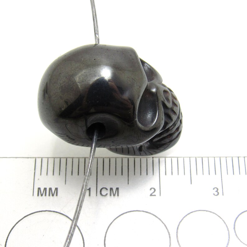 May include: A black skull bead with a hole for stringing. The bead is approximately 1 cm in diameter.
