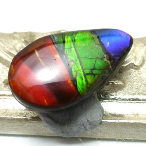 Könnte beinhalten: Ein tropfenförmiger, irisierender Opal-Edelstein mit einem roten, grünen und blauen Farbmuster.