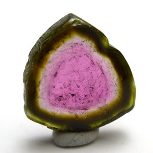 May include: A green, pink, and clear tourmaline crystal with a triangular shape. The crystal is cut in half, revealing the internal layers of the stone.