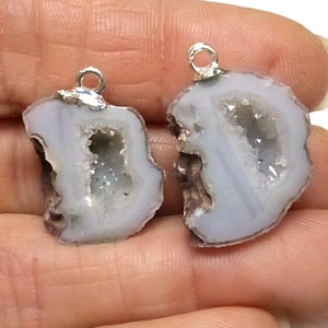 May include: Two white agate crystal pendants with silver jump rings. The crystals have a natural, rough exterior and a smooth, white interior with a small, clear crystal cluster in the center.