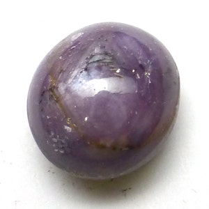 May include: A round, purple gemstone with a smooth, polished surface. The stone has a subtle shimmer and a few inclusions.