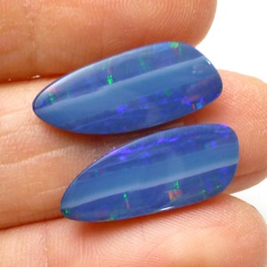May include: Two blue opal cabochons with iridescent flashes of green and red. The opals are oval shaped and have a smooth, polished surface.