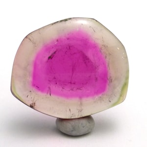 May include: A pink and white gemstone with a translucent, cloudy appearance. The gemstone is irregularly shaped and has a smooth, polished surface.