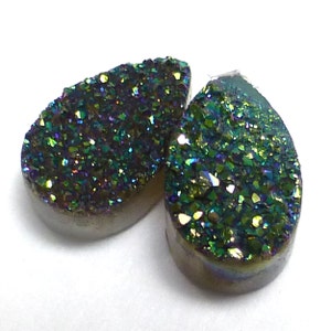 May include: Two teardrop-shaped iridescent green and purple agate cabochons with a sparkly, crystalline texture.