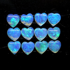 May include: Twelve heart-shaped opal cabochons in various shades of blue and green. The opals are arranged in four rows of three.