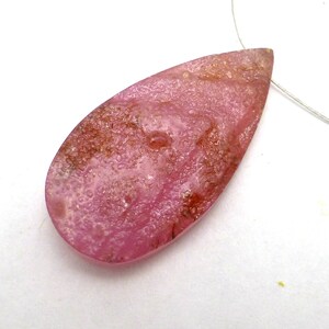 May include: Pink teardrop shaped gemstone with a textured surface and brown inclusions.