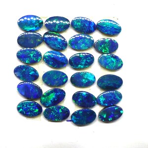 May include: A collection of 20 oval-shaped blue and green opals. The opals are arranged in rows on a white surface.