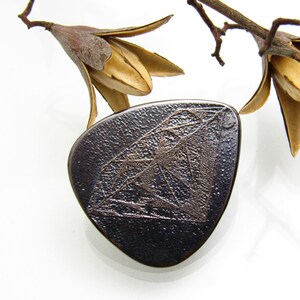 May include: A dark gray ceramic pendant with a raised diamond design. The diamond is outlined in a lighter gray color.