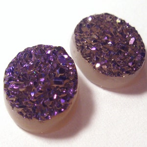 May include: Two round, purple and brown agate cabochons with a sparkly, iridescent finish. The cabochons are approximately 1 inch in diameter.