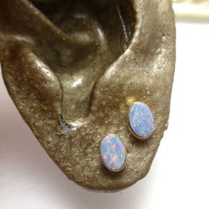 Könnte beinhalten: Ein Paar ovale Opal-Ohrringe in Gold gefasst. Die Opale sind hellblau mit schillernden Farbflecken.
