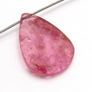 May include: A teardrop-shaped pink gemstone pendant with a translucent, slightly cloudy appearance. The pendant has a smooth, polished surface and is suspended from a silver wire.