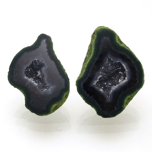 May include: Two polished agate geodes with a dark gray interior and a green outer edge. The center of each geode is filled with sparkling crystals. The geodes are displayed on a white background.