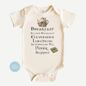 May include: A cream-colored short-sleeve bodysuit featuring a graphic of a teapot-shaped house and a list of meals including Breakfast, Second Breakfast, Elevensies, Luncheon, Afternoon Tea, Dinner, and Supper, with a small green parcel illustration.