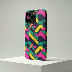 May include: A colorful phone case with a geometric pattern. The case features a vibrant design of pink, yellow, green, and navy blue shapes. The phone case is on a white surface.
