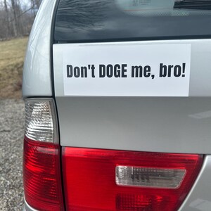 May include: A silver car with a white bumper sticker that reads "Don't DOGE me, bro!"