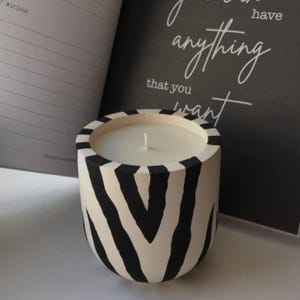 May include: A white candle with a black and white zebra print design on the container. The candle is sitting on a notebook with the text "You have anything that you want" written on it.